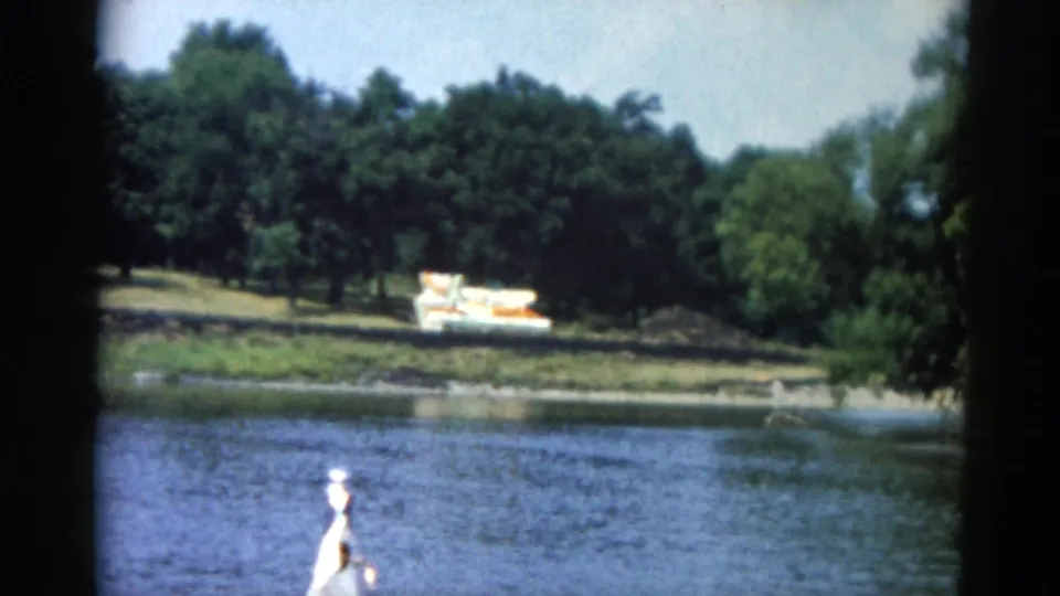 8mm footage at 0:02 — same 1962 Illinois river scene with person at bow and a colorful boat beached on the far tree-lined bank.