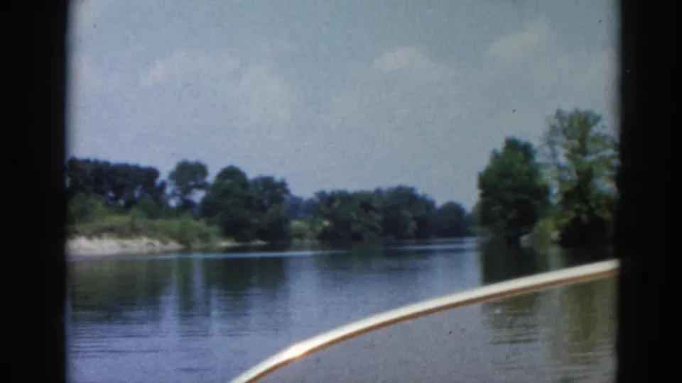 8mm home movie, c.1962 Illinois — forward river POV from motorboat, low wooded banks ahead, partly cloudy sky, white bow edge in frame.