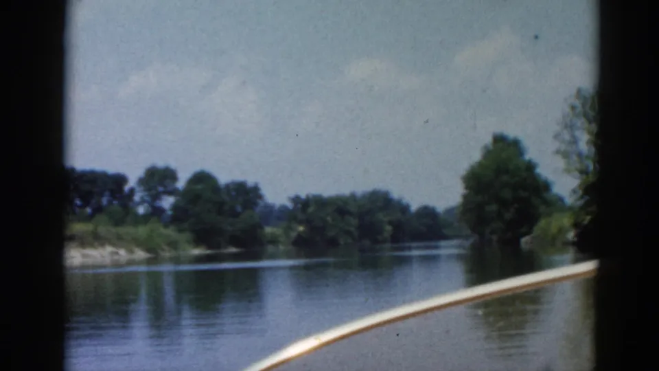 Final frame of 8mm Illinois river clip, c.1962 — open waterway ahead, tree-lined banks, white boat bow edge, cloud-tinged sky.