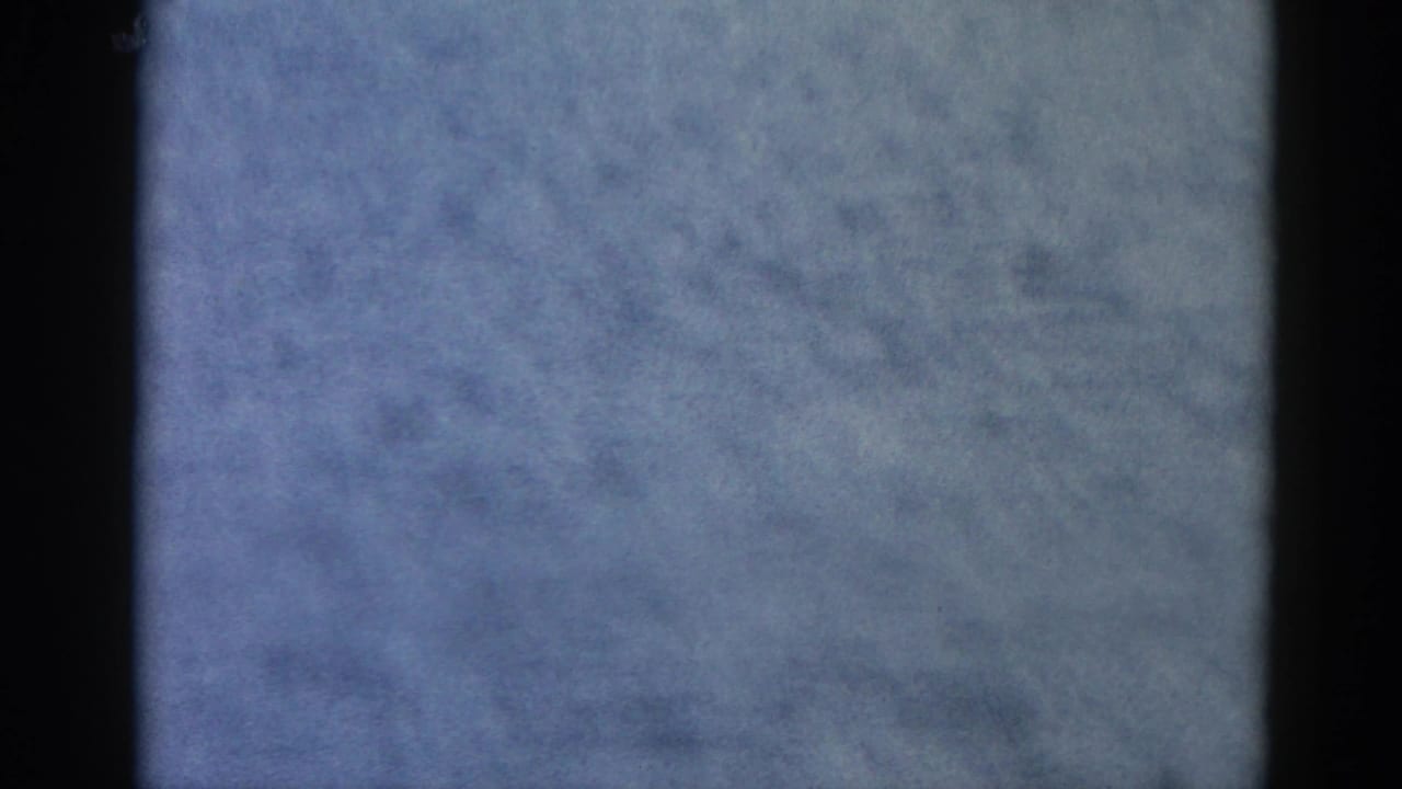 Heavily underexposed 8mm frame; overcast sky fills most of the image with film grain and a dark border.