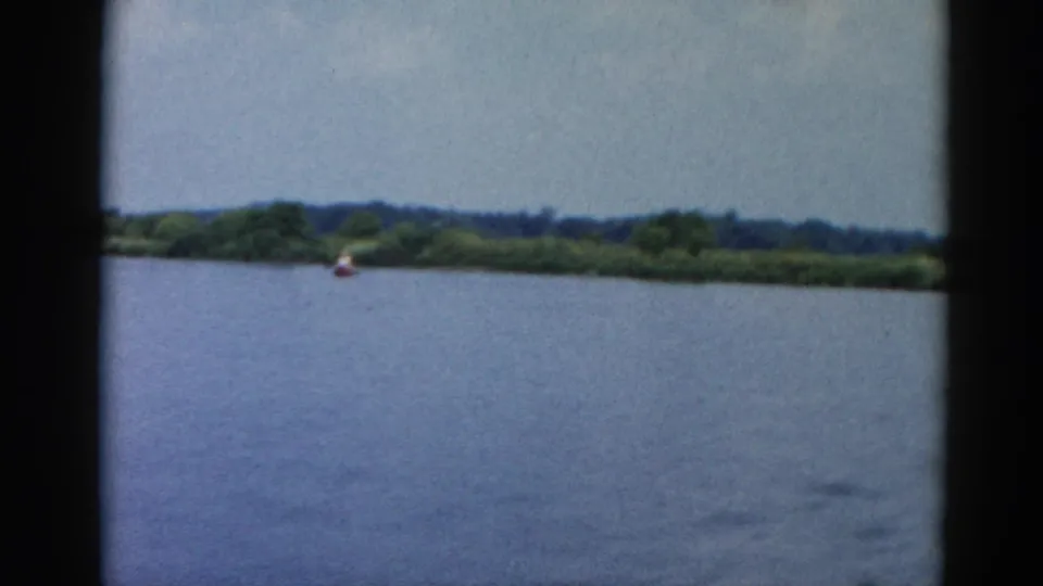 Expansive open lake water with a low treeline on the far shore and a small figure in a distant boat, Illinois, circa 1962, 8mm home movie.