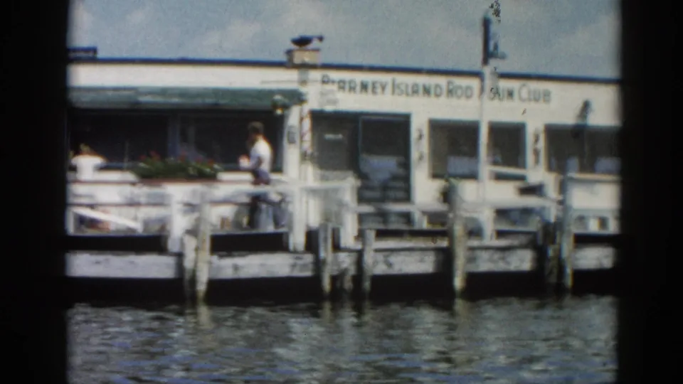Continuation shot of the Blarney Island Rod & Gun Club wooden pier, Illinois circa 1962; a person stands on the dock deck to the right of the building.