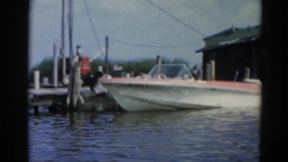 White speedboat with red trim moored at a waterway dock, Illinois circa 1962; a partial boat shed structure is visible at the right edge of frame.