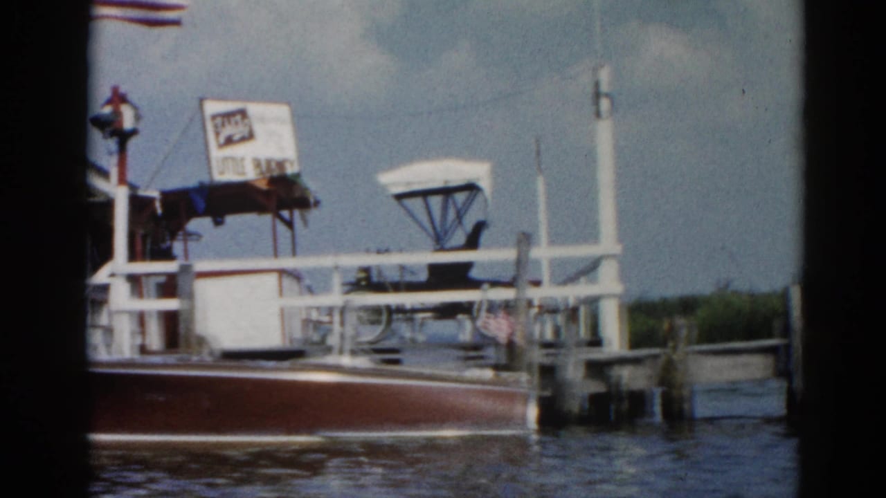 Ferry dock white building at a waterfront club; American flag and signage visible; wooden boat in foreground.