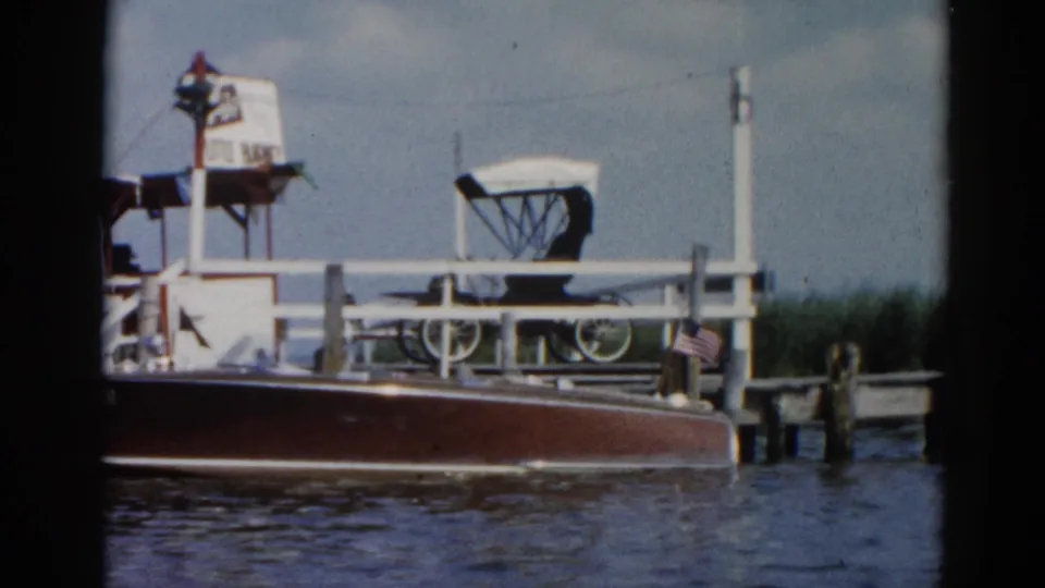 Close shot of a classic mahogany motorboat with steering wheel at a dock with 'Little Blarney' signage, Illinois waterfront circa 1962.