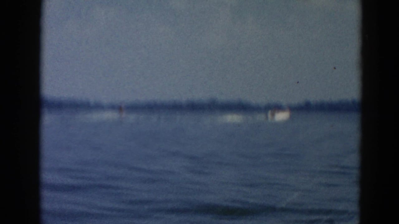 Lake view through a window frame, open water with distant shore; small boat or wake visible in the far distance at right.