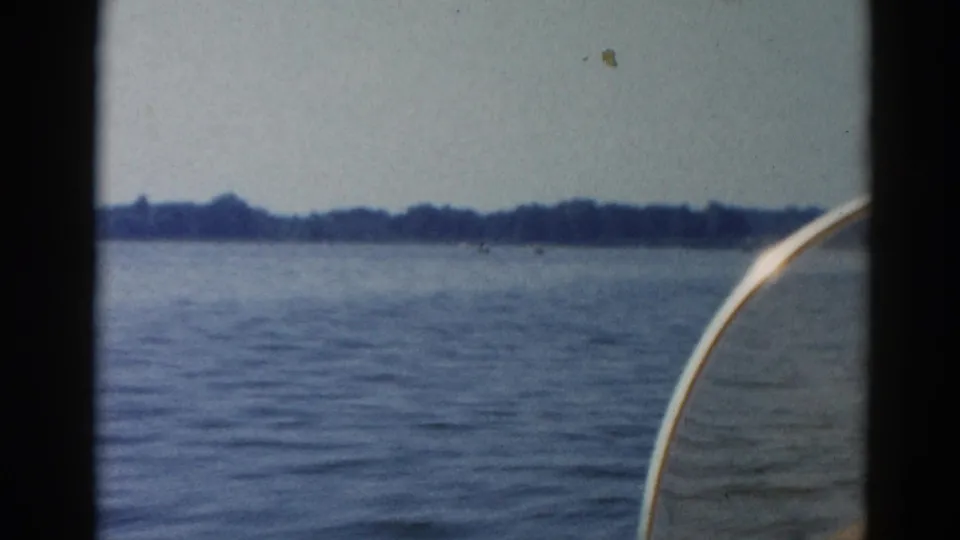 Wide shot of open Illinois lake under overcast sky, circa 1962, with distant flat treeline and partial white boat hull in foreground.