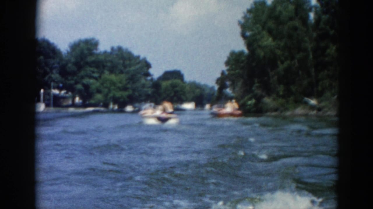 Wide river with several small motorboats underway and tree-lined shores, filmed from a moving boat