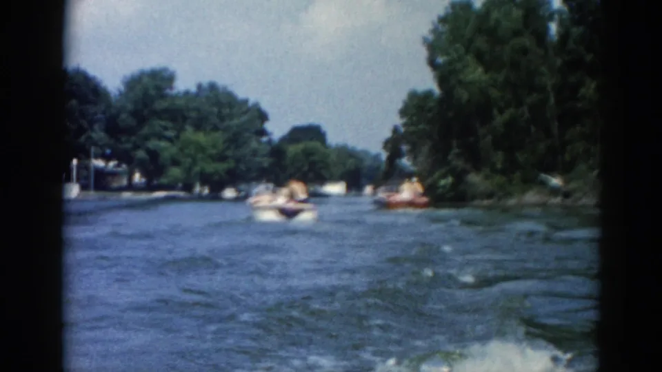 8mm footage from 1962 Illinois showing multiple motorboats on a wide river with dense tree-lined banks and a pale blue sky