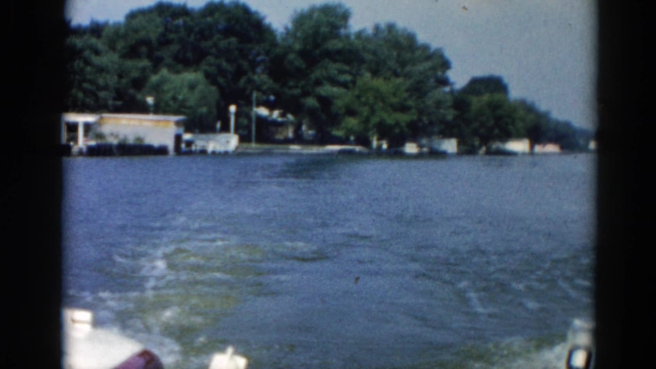 1962 Illinois waterway from a moving motorboat showing open choppy water, a small structure on the far shore, and dense summer treeline