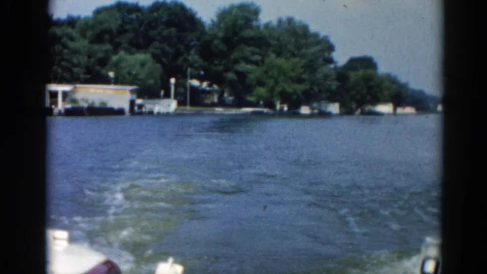1962 Illinois waterway from a moving motorboat showing open choppy water, a small structure on the far shore, and dense summer treeline