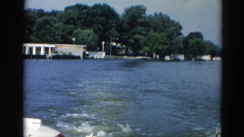 1962 Illinois river scene showing a low boathouse or dock building among dense summer trees along a calm waterway