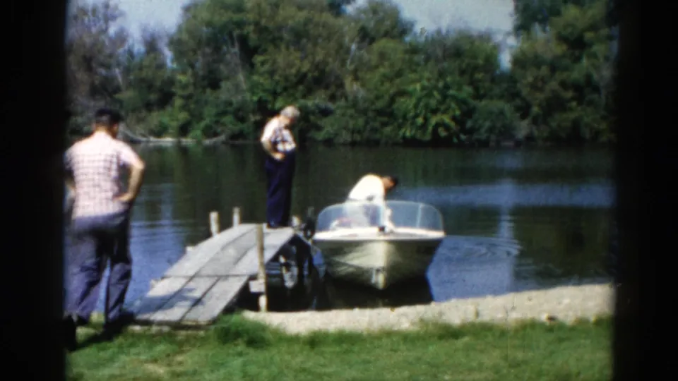 Three men at a small lake dock with a motorboat; a third man in a plaid shirt joins from the left, 8mm film, Illinois, circa 1962.