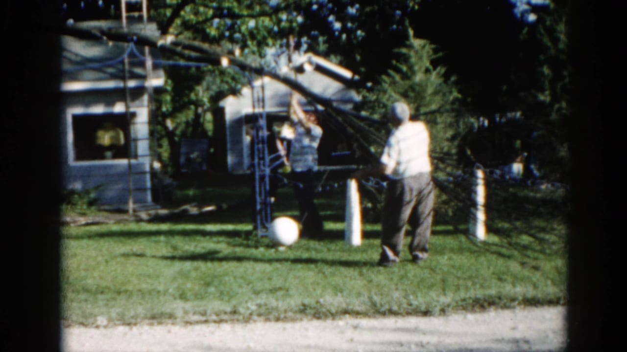 Two men operating a makeshift pulley apparatus in a suburban Illinois backyard, circa 1962, shot on 8mm color film.