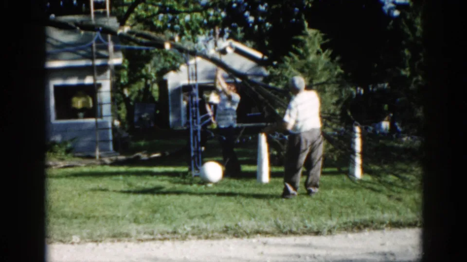 Two men operating a makeshift pulley apparatus in a suburban Illinois backyard, circa 1962, shot on 8mm color film.