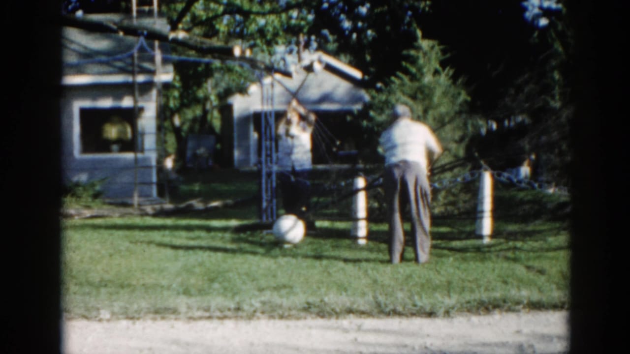 Man in light shirt and dark trousers at a makeshift pulley apparatus in a suburban Illinois backyard, likely circa 1962, 8mm film.