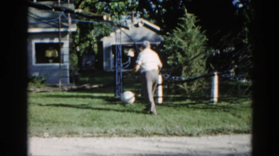 Man in light shirt crossing a green suburban lawn near a metal pulley frame, likely Illinois circa 1962, 8mm color film.