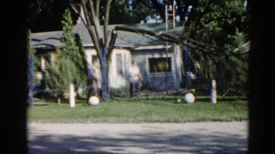 8mm home movie, c.1962, Illinois: a man in a white shirt stands in the foreground of a suburban yard while a large felled tree rests against the single-storey ranch house behind him.