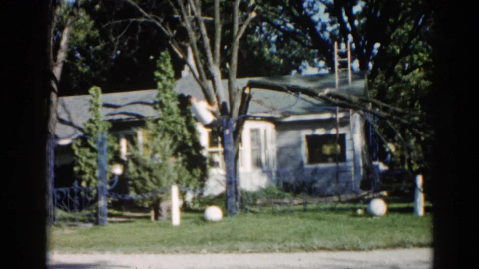 Two figures near a large tree in a grassy Illinois suburban yard with period pipe fence and white yard ornaments, 8mm film circa 1962.