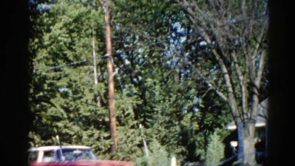 Final 8mm frame from c. 1962 Illinois showing a red period automobile, utility pole, and leafy suburban trees at the edge of the backyard property.