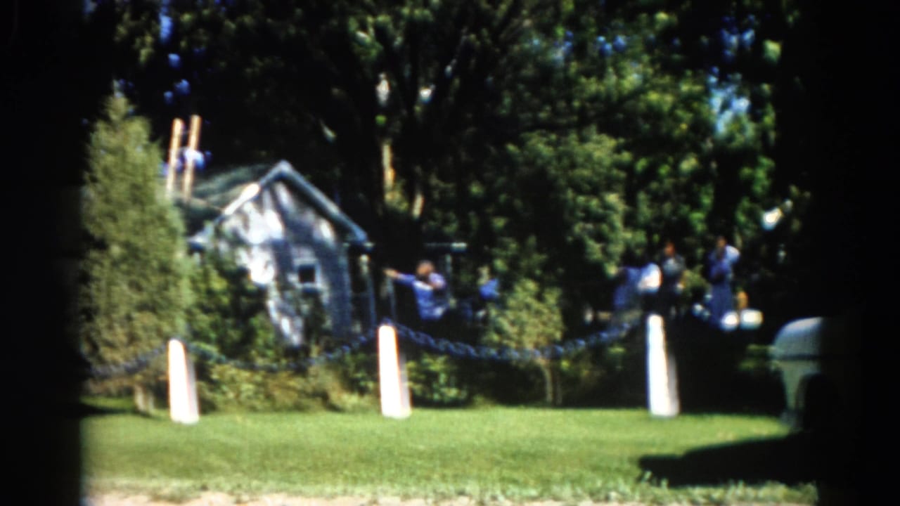 Figures working in and around large trees beside a modest two-story house, with green lawn visible.