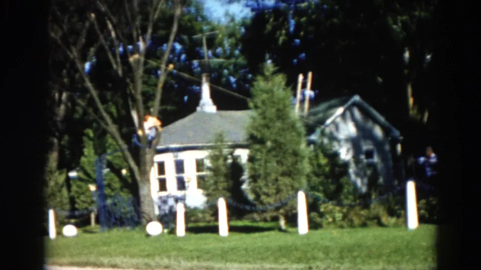 Wider view of a rural Illinois property showing a two-story white house, figures trimming tall trees, and white lawn stakes in foreground, circa 1962.