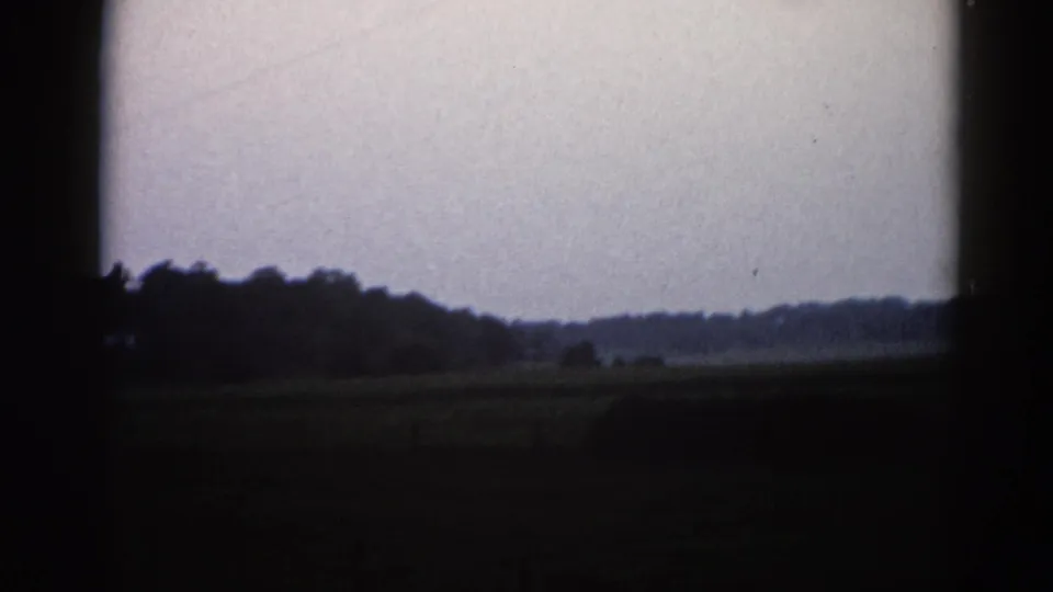 Illinois rural landscape on 8mm film, c. 1962; flat field and tree-line horizon under pale grey sky with film-edge vignetting and grain.