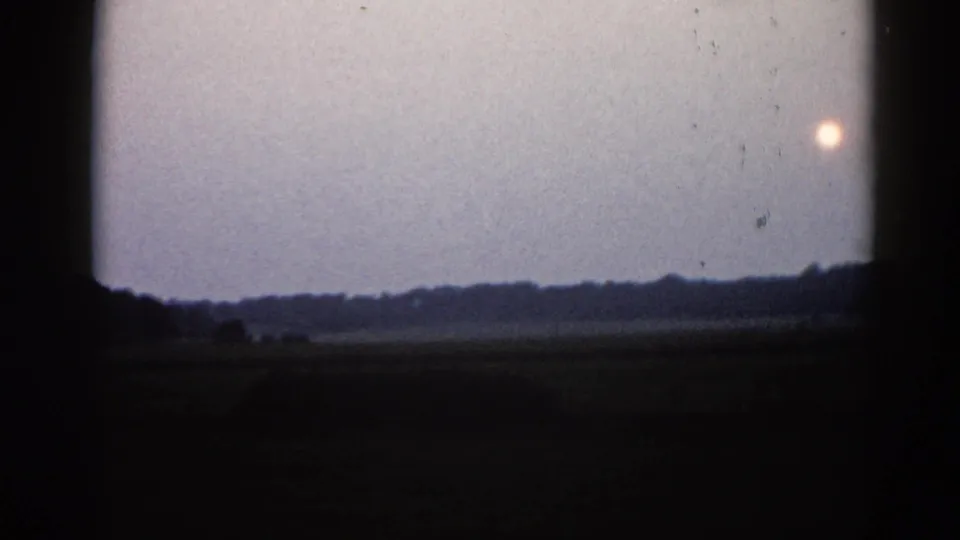 Final frame of 1962 Illinois 8mm clip; bright sun orb appears in the upper right against a cool grey sky, tree line reduced to a thin dark strip below.
