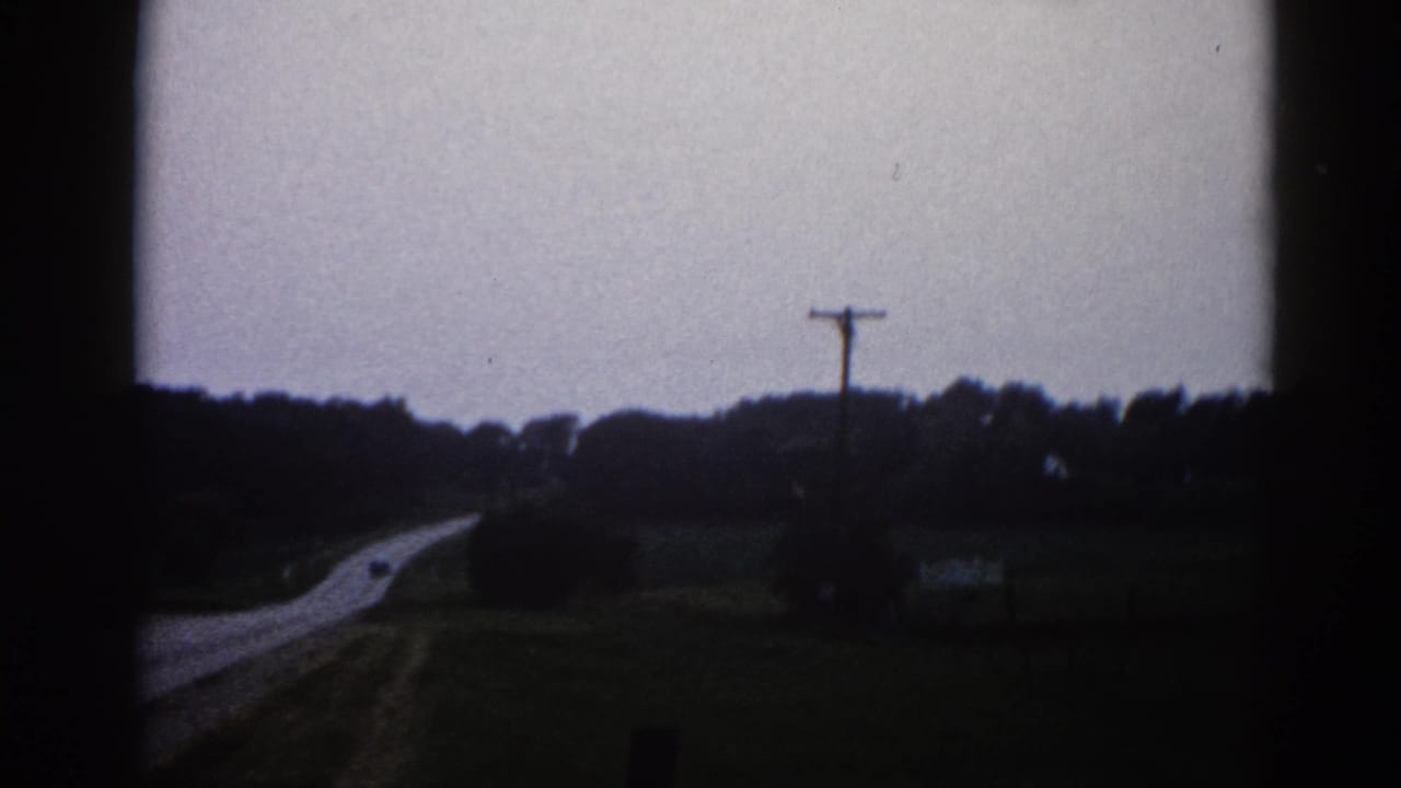 Rural road receding into the distance with a utility pole, treeline, and overcast sky, shot on 8mm film.