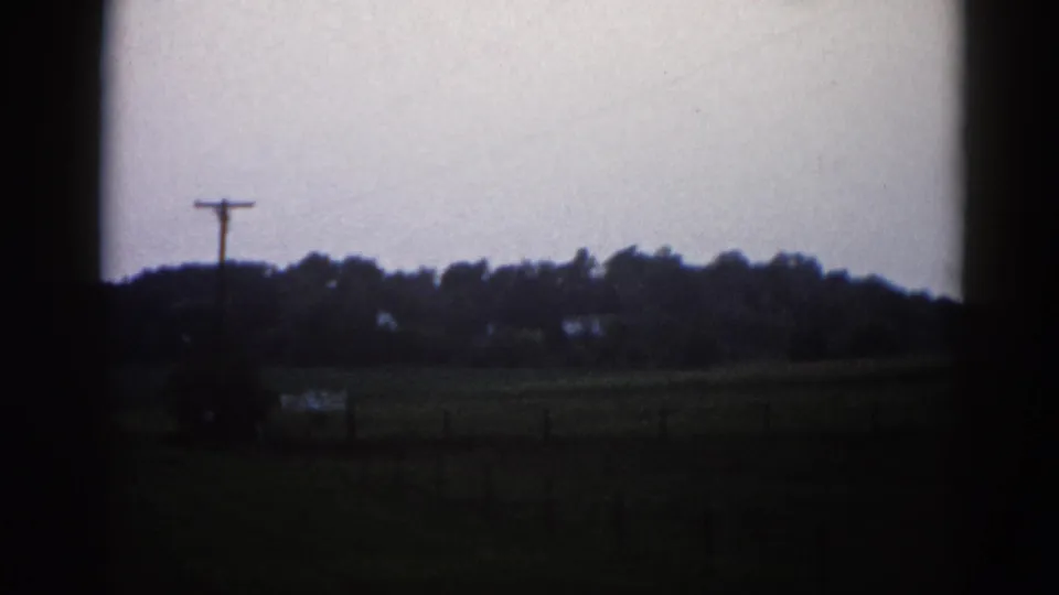 Roadside pan of open farmland in rural Illinois, 1962 — utility pole at left, distant treeline, overcast sky, possible fence line, on 8mm film.