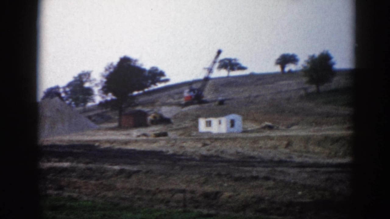 8mm frame, c.1962, Illinois — slow pan reveals white site structure and lattice-boom crane amid graded earth and large gravel mound.