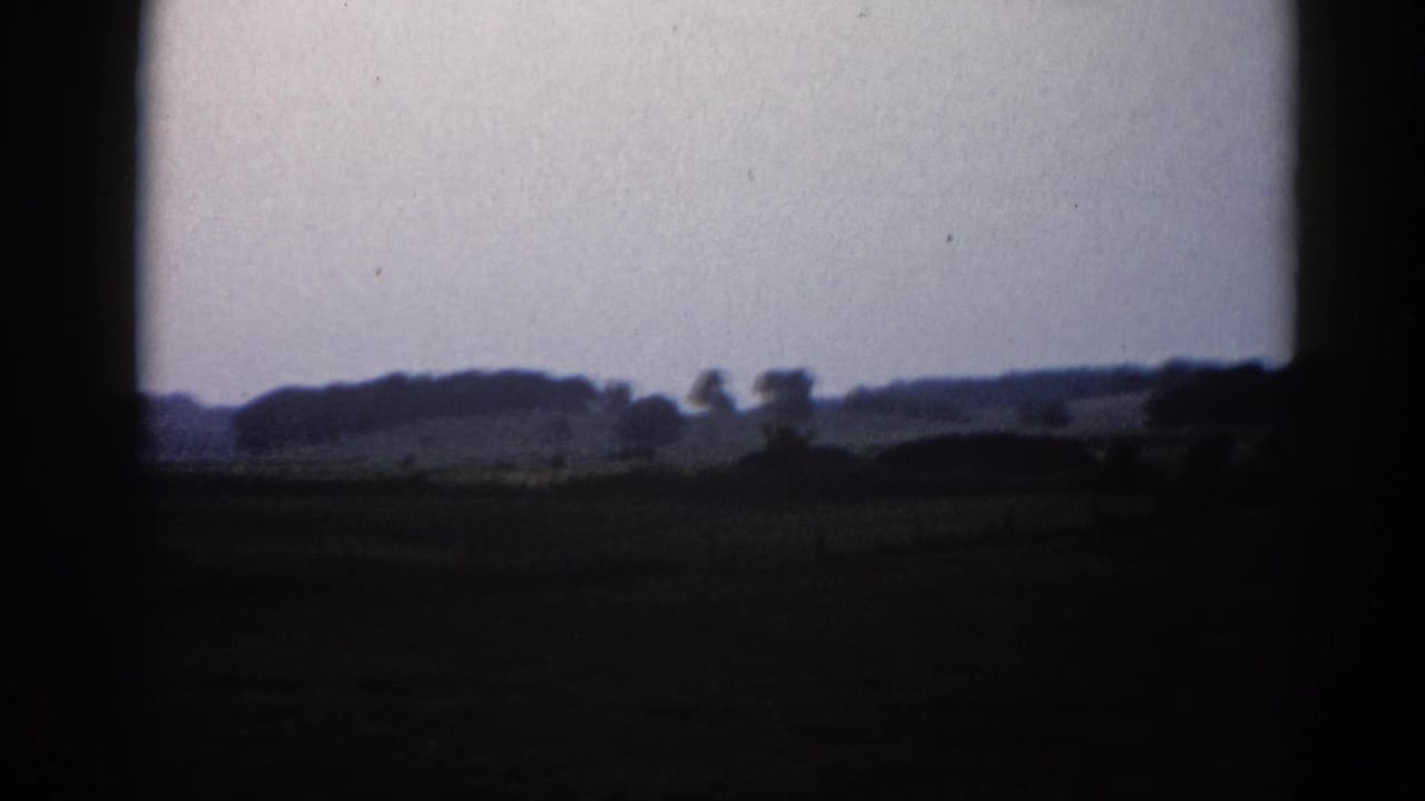 Rural landscape with overcast sky and tree-lined horizon, filmed on 8mm with heavy edge vignetting.