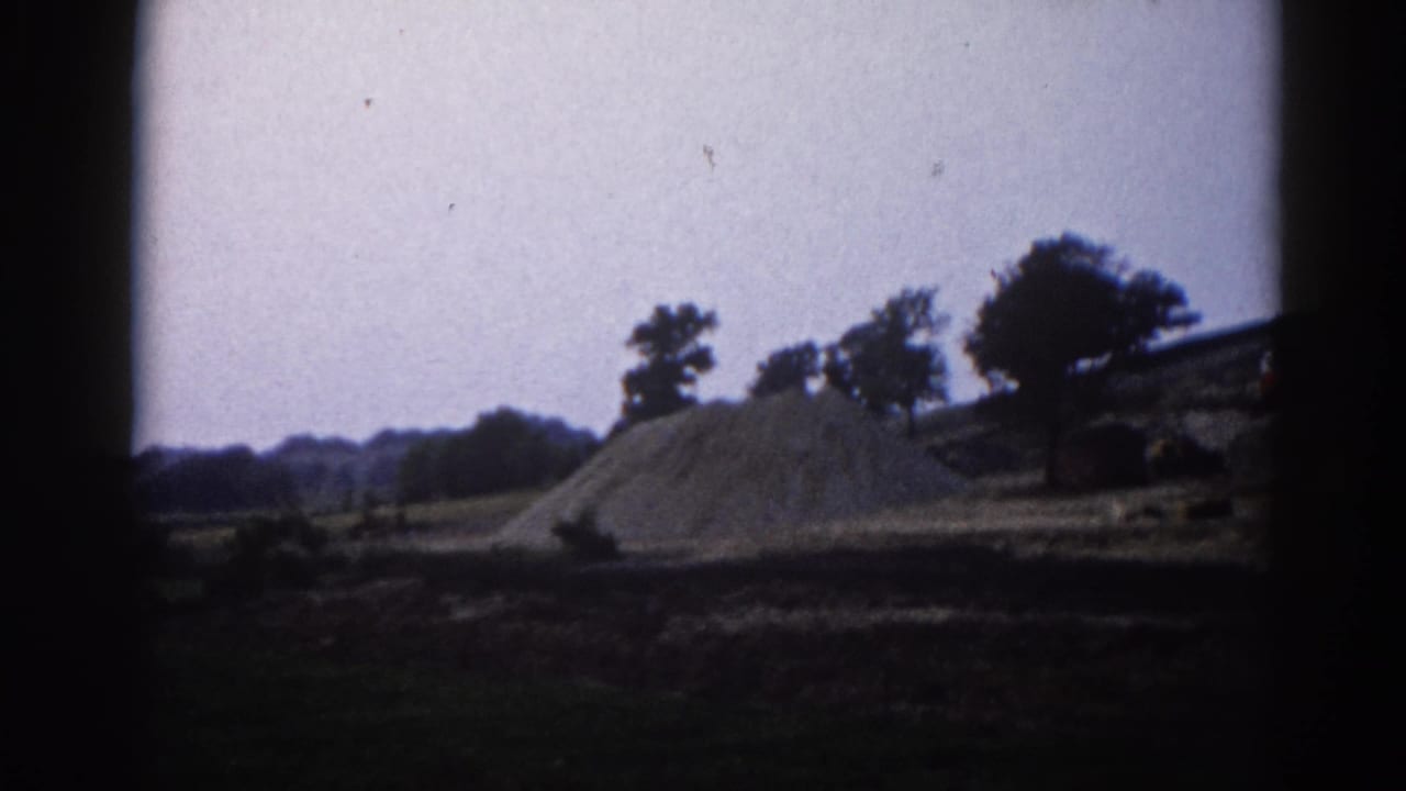 Large gravel pile on bare earth with trees along the horizon under overcast sky, filmed on 8mm with heavy vignette borders.