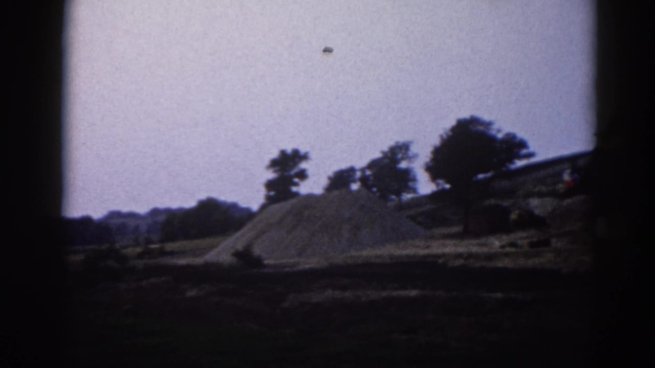 Gravel mound and treeline at a rural construction site filmed on 8mm with characteristic vignette; similar framing to opening frame.