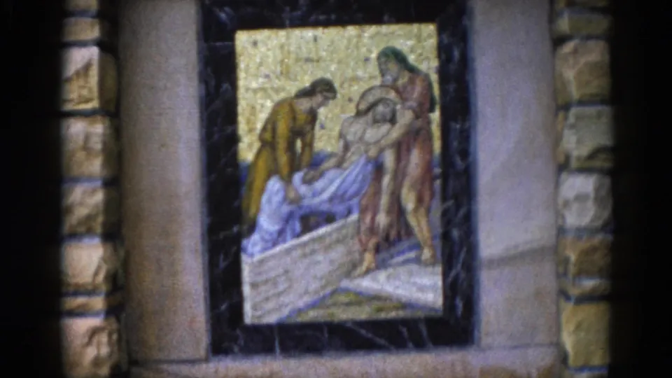 Closer 8mm frame of the Deposition mosaic — ochre and blue-grey robed figures lowering a recumbent figure — with gold tesserae background and stone columns, Illinois church interior, circa 1962.