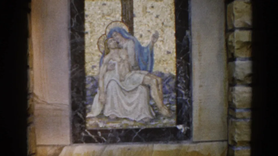 Closing 8mm frame from 1962 Illinois church footage; Pietà mosaic with blue-robed Mary and white-robed Christ in gold-tile setting, stone walls flanking.