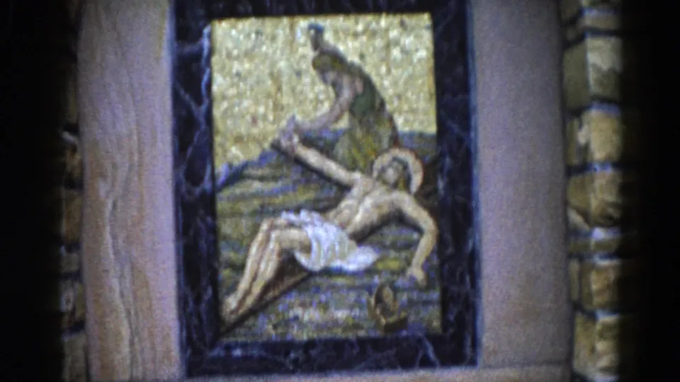Outdoor devotional mosaic depicting a Lamentation scene: dark-robed mourning figure over a semi-recumbent haloed figure, set in dark marble within a rough stone surround, Illinois c.1962.