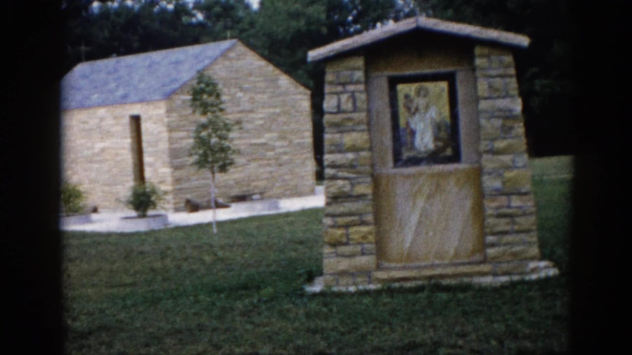 Close view of a framed religious mosaic on a stone pillar outside a small cut-stone chapel, Illinois, 1962, 8mm home movie.
