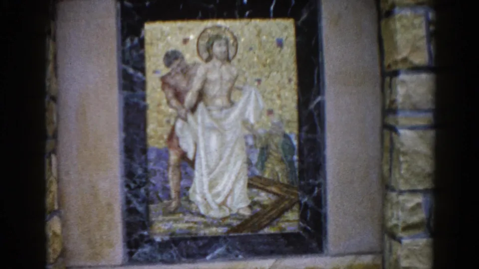 8mm film frame, 1962, Illinois: mosaic showing a halo-bearing figure in white robes and a companion figure against a gold tessellated background, mounted in dark marble within a stone church wall.