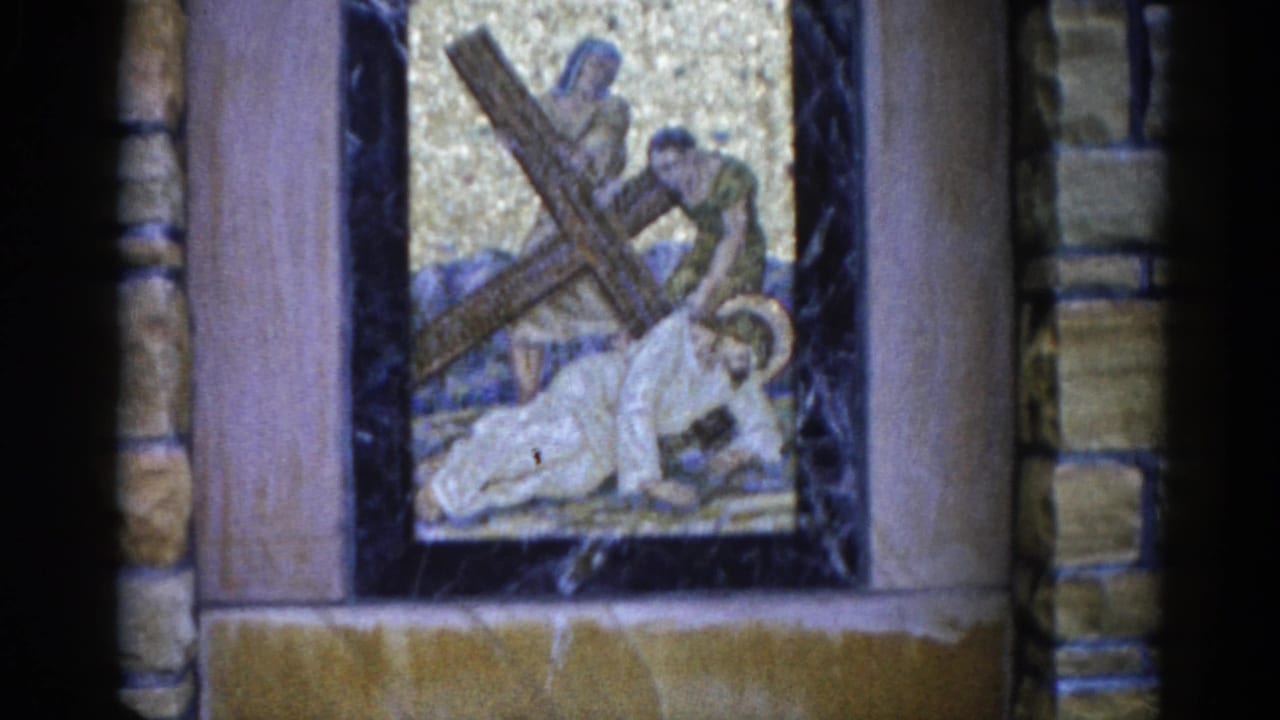 Mosaic panel showing a haloed figure kneeling under a wooden cross, flanked by two standing figures, against a gold tessellated background in a stone-framed church wall.