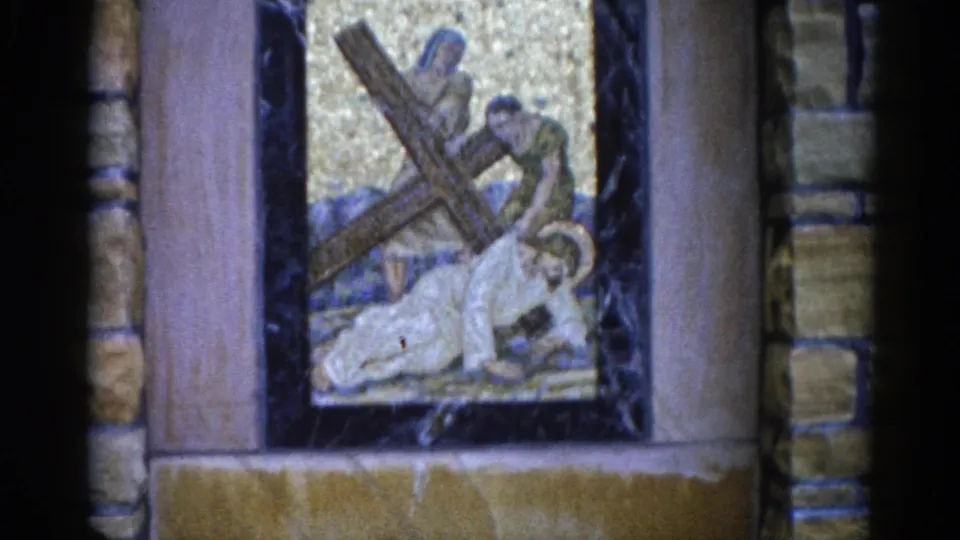 8mm home movie from 1962 Illinois: Passion mosaic showing a haloed figure kneeling beneath a wooden cross, attended by two others, gold tesserae background within dark marble and buff stone framing.