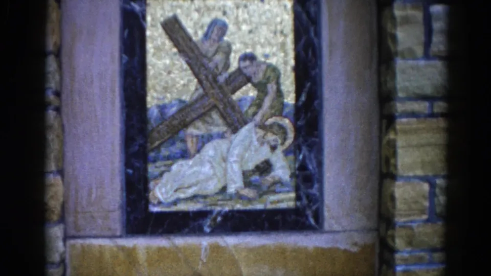 Third 8mm frame from 1962 Illinois church: Passion scene mosaic showing a haloed figure under a wooden cross with a standing attendant, gold background framed by dark marble and warm stone pilasters.