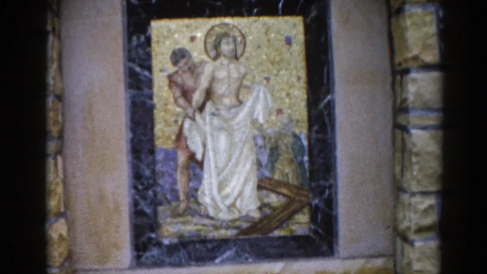 Fourth 8mm frame from 1962 Illinois church: mosaic panel of a standing haloed figure in white drapery with an attendant, gold tessellated background within dark marble and buff stone framing.