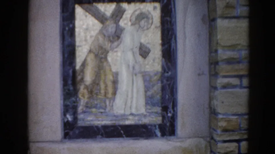 8mm footage from 1962 Illinois church: mosaic depicting Jesus carrying the cross with a companion figure, dark marble border, stone block wall visible.