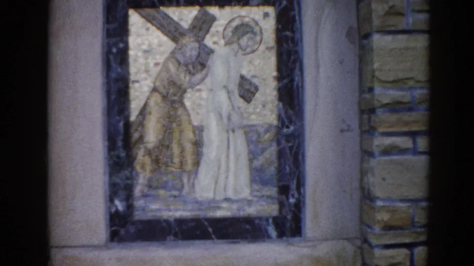 Final frame of 1962 Illinois church sequence: mosaic of Jesus carrying the cross alongside a companion figure, gold tesserae, dark marble border.