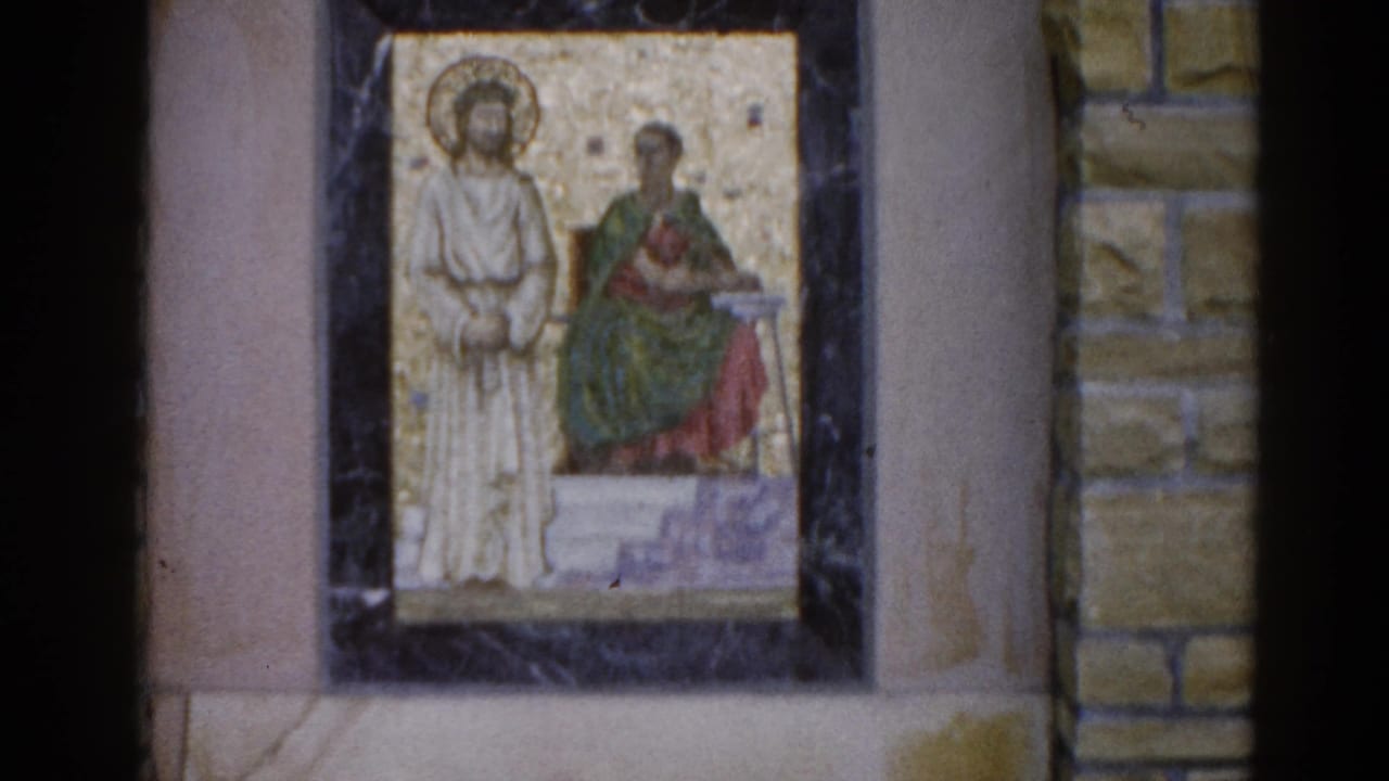Two religious mosaics on a stone church wall, each in a dark marble frame; left mosaic shows two haloed figures on a gold background.
