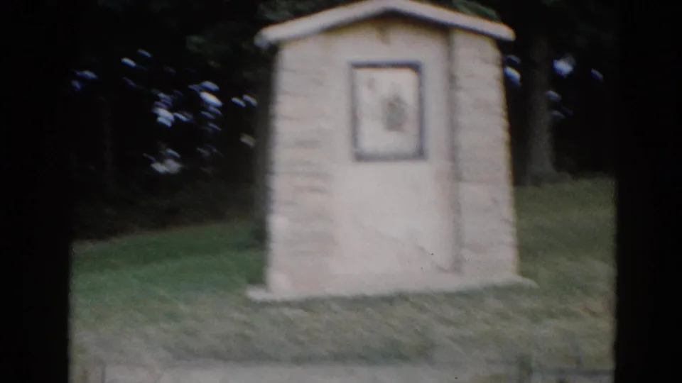 Small concrete or limestone outdoor shrine on a grass lawn with tree backdrop, Illinois, circa 1962, shot on 8mm film.