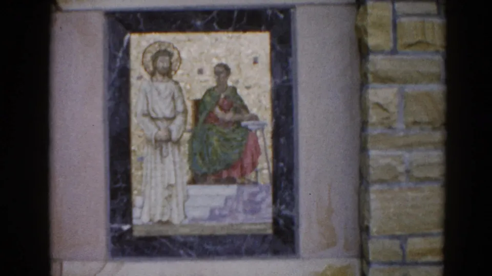 Byzantine-style religious mosaic in a dark marble-like frame mounted on a tan stone wall, two haloed figures, Illinois circa 1962, 8mm film.