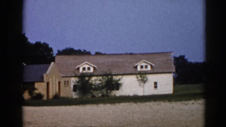 1962 Illinois farmstead: long white clapboard farmhouse with twin dormer windows against a rich blue dusk sky, photographed on 8mm film.
