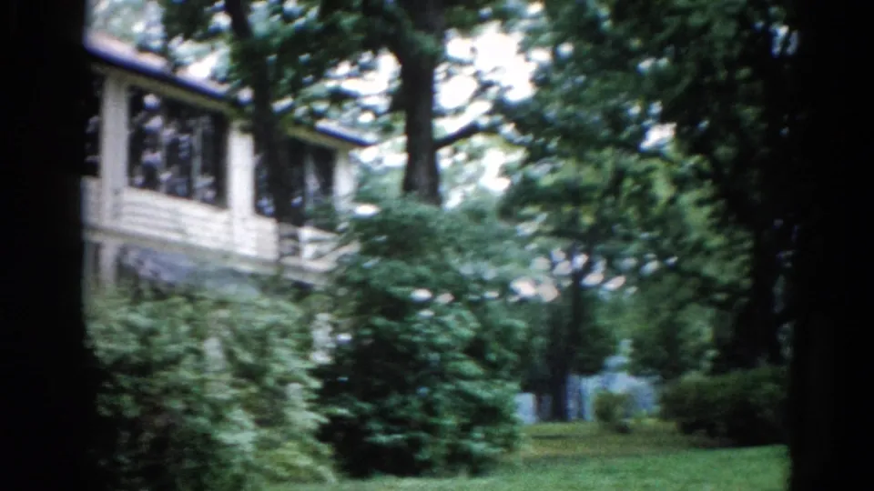 Pan revealing manicured summer lawn and mature trees, house receding to left edge of frame — 8mm home movie, Illinois, 1962.